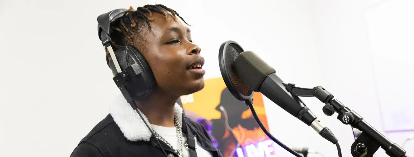 Youngster wearing headphones singing into a microphone on a stand with a pop guard