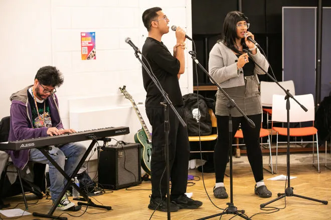 Two young people singing into microphones and a youth worker playing the keyboard