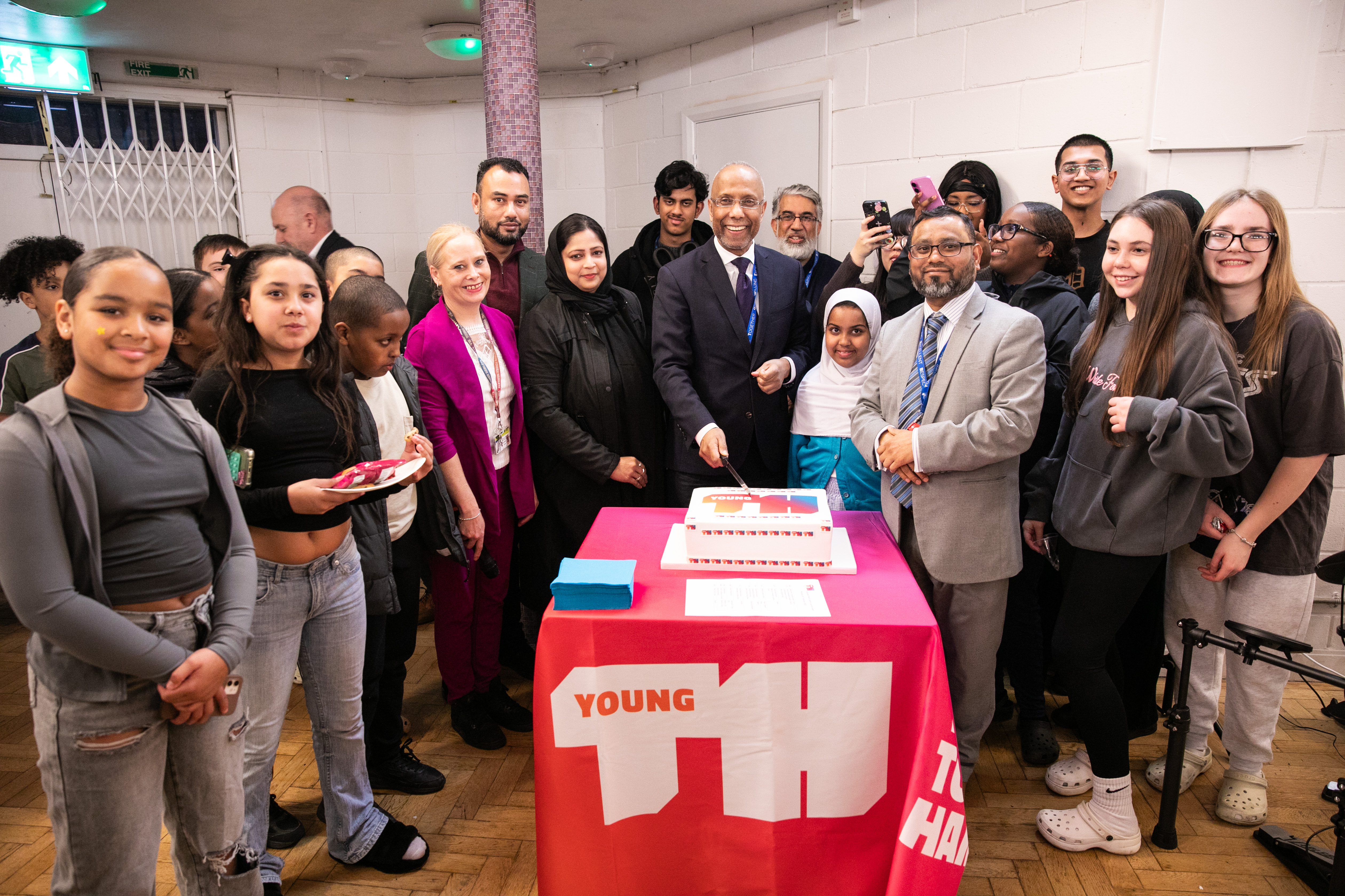 The Executive Mayor Lutfur Rahman cuts a cake to celebrate the launch of Young Tower Hamlets at Samuda Youth Center, surrounded by smiling youngsters