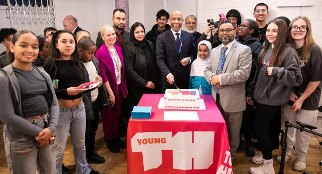 The Executive Mayor Lutfur Rahman cuts a cake to celebrate the launch of Young Tower Hamlets at Samuda Youth Center, surrounded by smiling youngsters