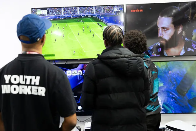 Youth Worker playing PlayStation 5 with a group of Young People